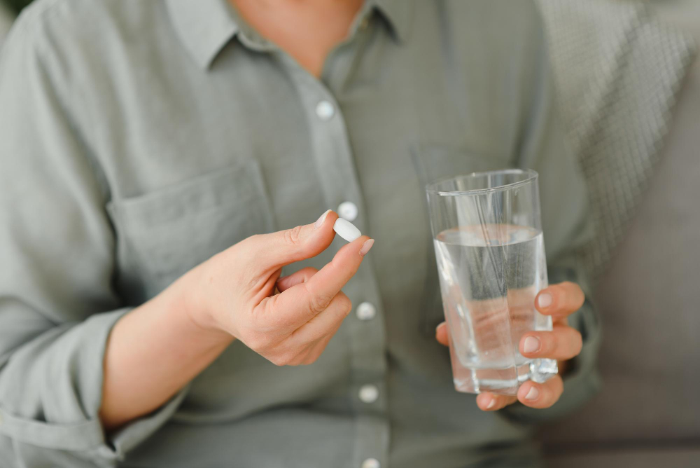 Close-up of a person holding a pill and a glass of water, preparing to take medication